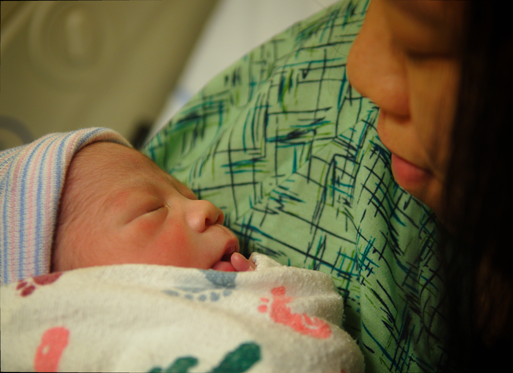 A first-time mother holds her swaddled newborn baby close, beginning to bond in the early hours after birth.