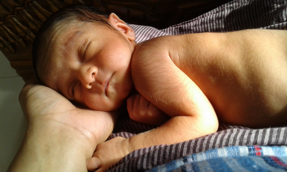 A newborn baby sleeping soundly, curled up while cradled in the mother’s hand – illustrating the precious but unpredictable sleep of a newborn.